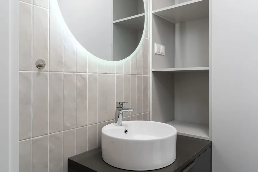 Backlit round mirror above a basin with a recessed niche beside it, borrowed light in a compact Exeter bathroom