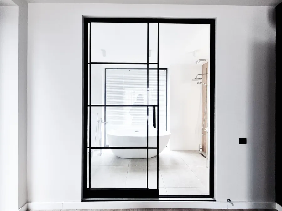 A black framed Crittall-style glass screen enclosing a freestanding bath in a bathroom