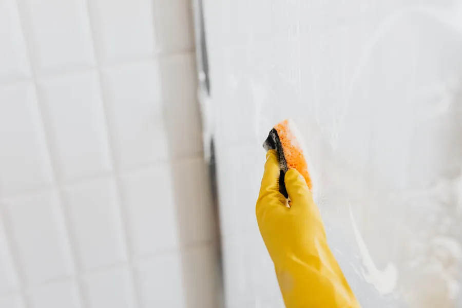 A gloved hand cleaning a shower glass panel in an Exeter bathroom