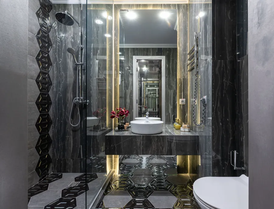 A frameless glass shower panel in a dark marble bathroom, an Exeter luxury bathroom installation