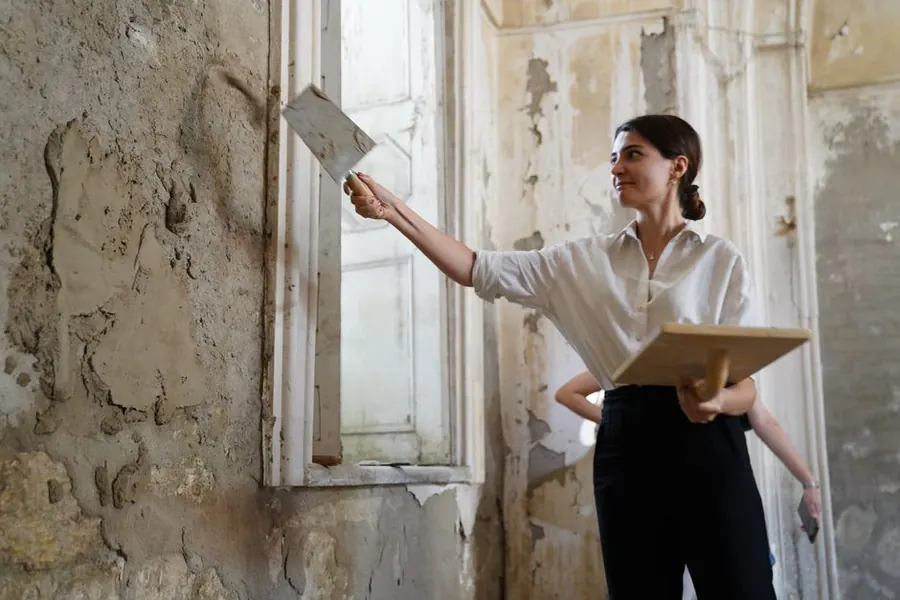A plasterer working on bare lime plaster in a stripped period room, the substrate a solid-walled Exeter bathroom is built against