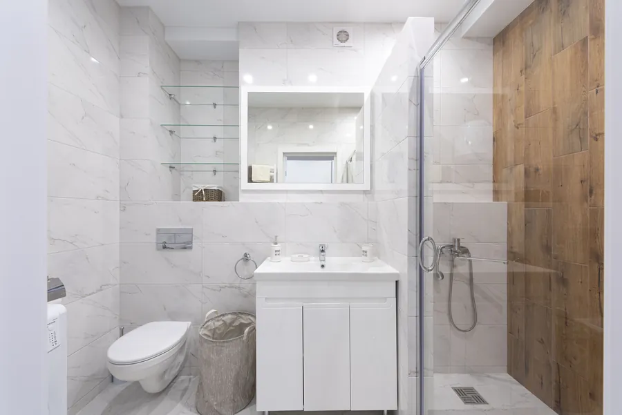 A sliding shower enclosure in a marble-tiled bathroom with a wall-hung basin