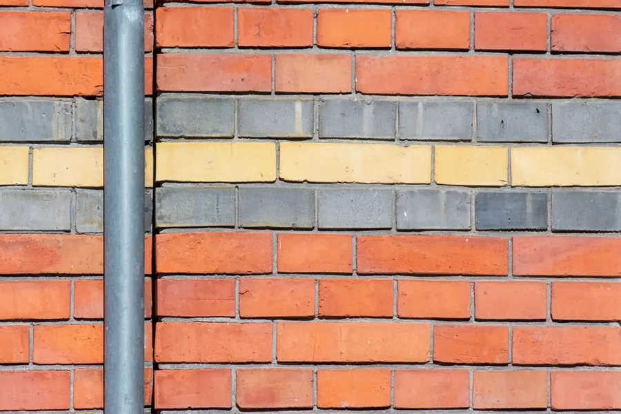 A waste pipe running down a brick wall, the external drainage route that decides where a WC can sit