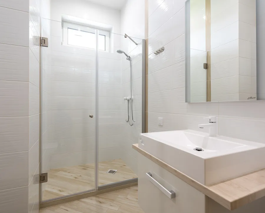 A minimal-framed toughened glass shower door in a white tiled bathroom, showing the slim wall channel