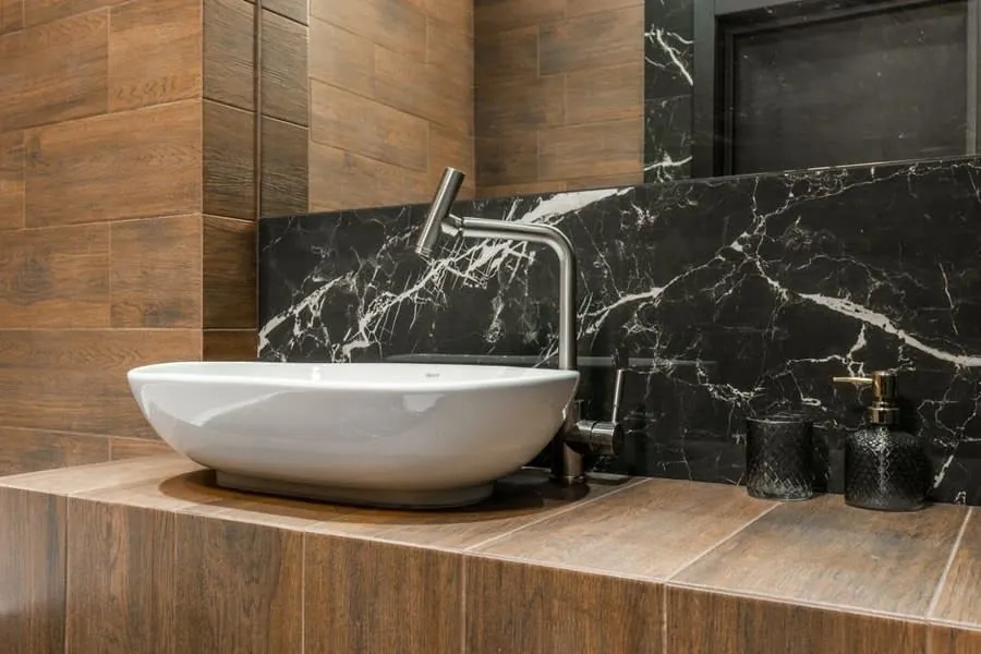 Black marble splashback behind a white vessel basin on an oak shelf