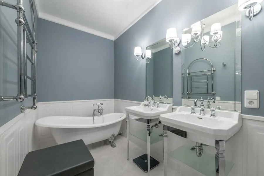 Period bathroom design with a roll-top bath and twin pedestal basins in a soft blue-grey scheme