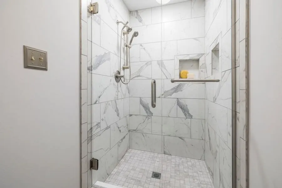 Marble-tiled shower enclosure with a recessed shelf and glass screen