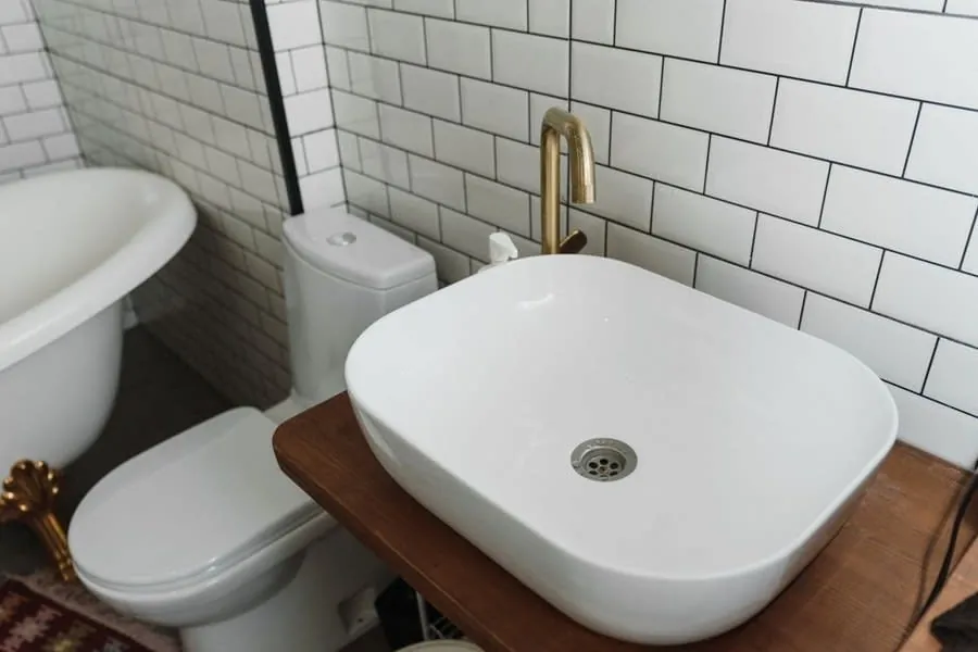 White metro wall tiling with a tall brass basin tap and counter-top basin