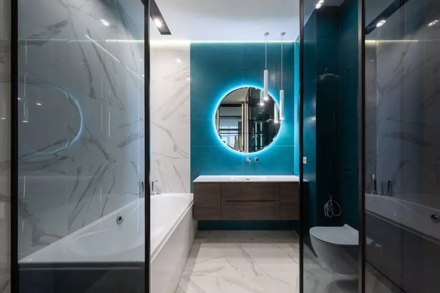 A round backlit mirror on a marble wall in a softly lit bathroom