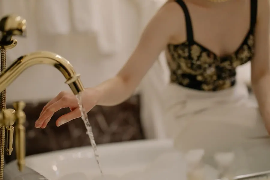 Testing the water while a bath fills from a gold floor-standing filler