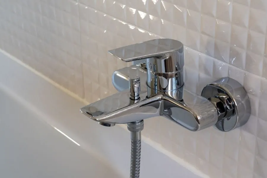 A chrome bath-shower mixer valve on white tiling