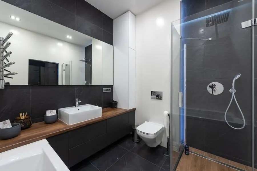 A backlit LED bathroom mirror above a wall-hung vanity with ceiling downlights