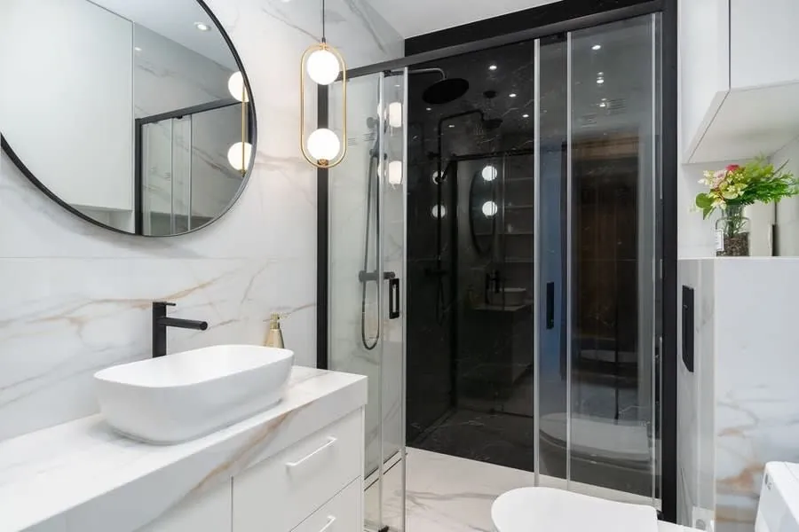 Pendant lights hanging beside a round mirror in a marble bathroom