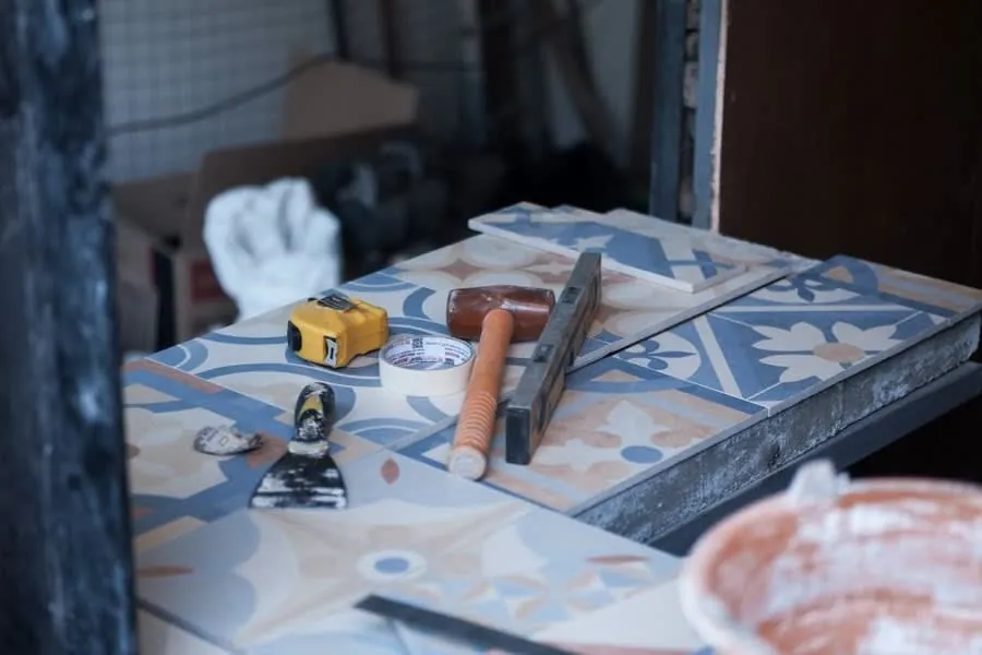 Patterned floor tiles laid out beside a tape measure, trowel and adhesive