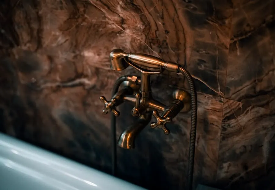 An aged brass bath mixer with hand shower mounted on dark marble