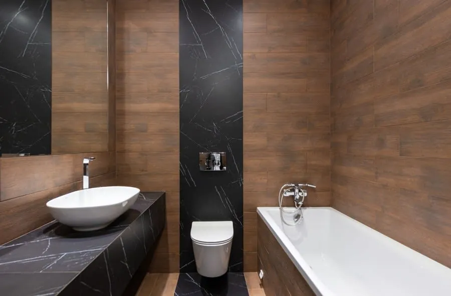 Built-in bath against a tiled wall in a compact wood and marble bathroom