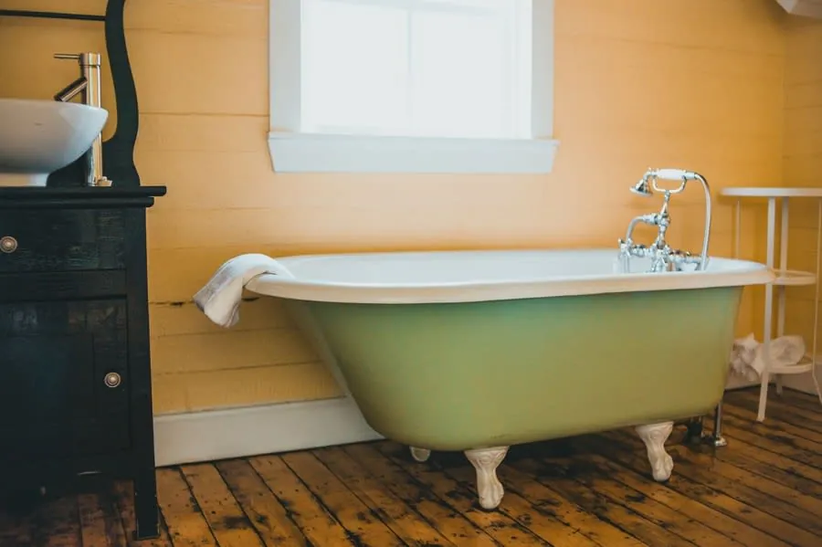 Green cast iron clawfoot bath on old floorboards in a period bathroom