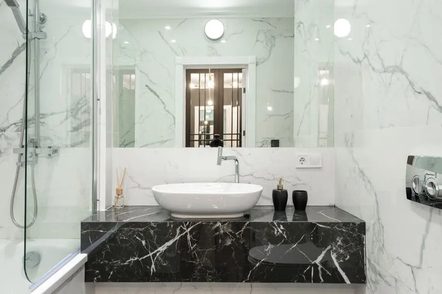 A white countertop basin with tall mixer on a black marble vanity top
