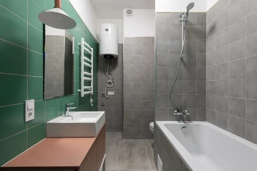 A wall-mounted electric shower unit above a bath on a green tiled wall
