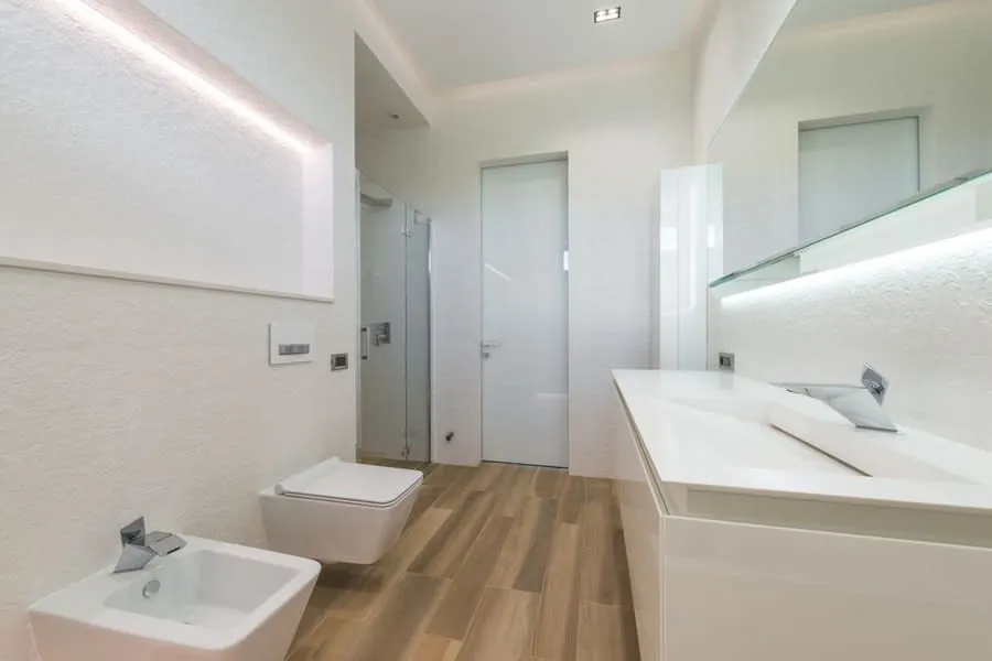 An en-suite with a bath, wall-hung WC and pale wood-effect flooring