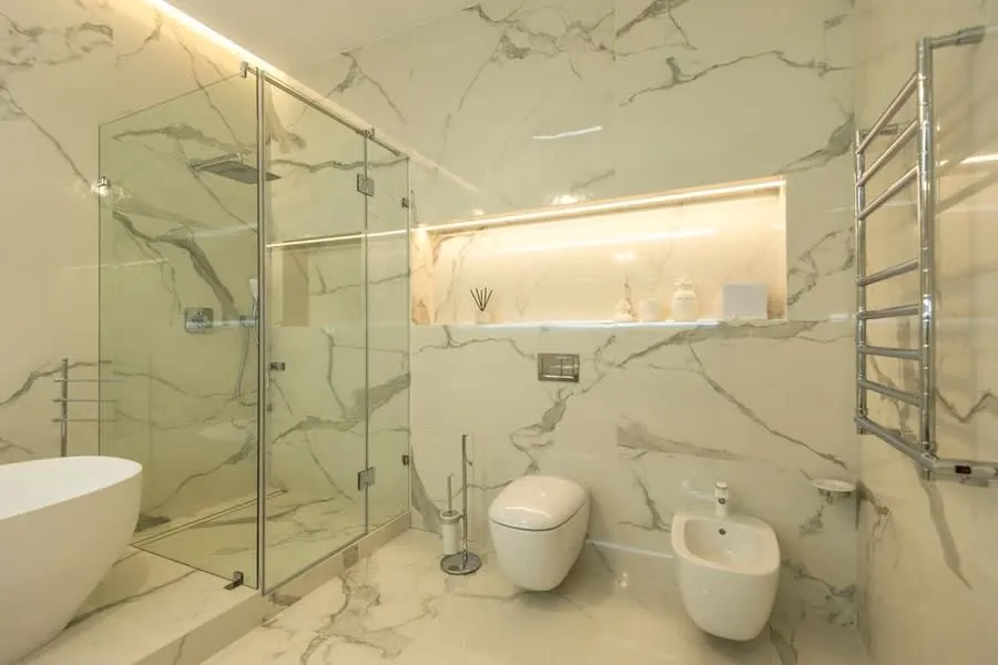 A frameless glass shower enclosure in a marble-lined bathroom
