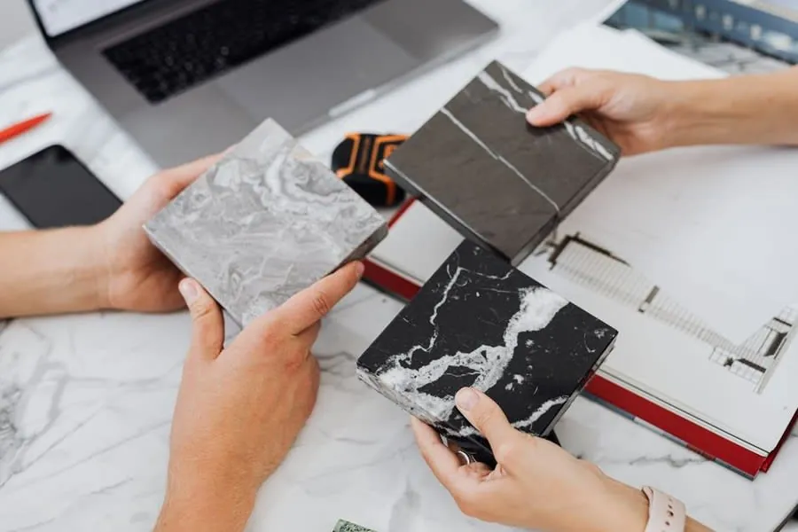 Hands comparing grey and black marble tile samples over a project plan