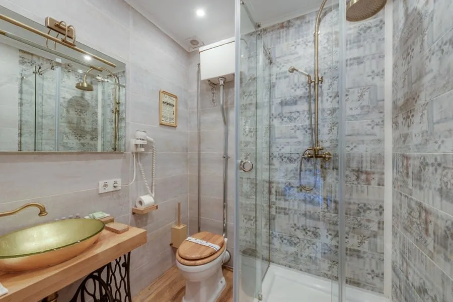 A bathroom combining brass fittings with a glass screen and timber, finishes chosen deliberately