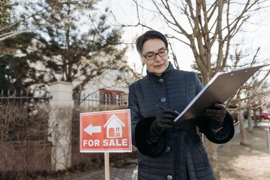Estate agent making notes beside a For Sale board outside a house