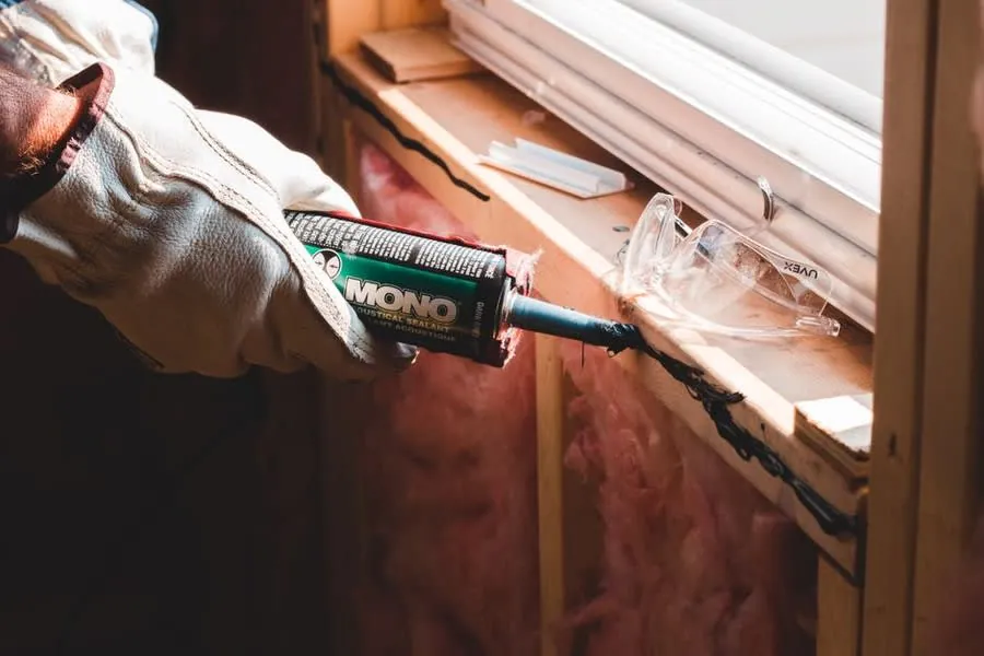 A gloved hand running a bead of sealant along a joint during refurbishment work