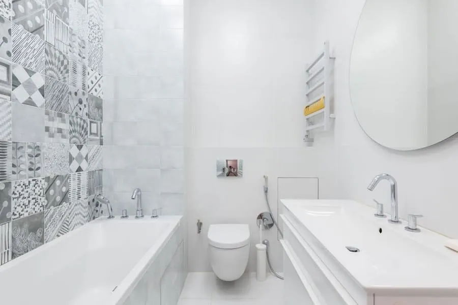 Patterned feature tiling beside a bath, with a wall-hung WC and round mirror