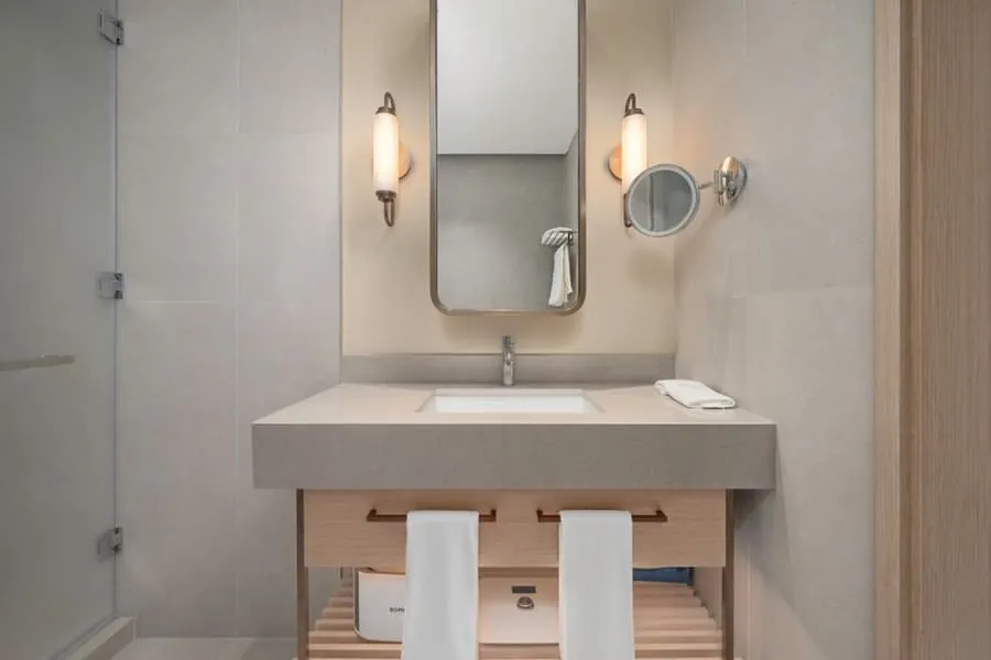 Stone vanity with flanking wall lights and a glass screen in a small bathroom