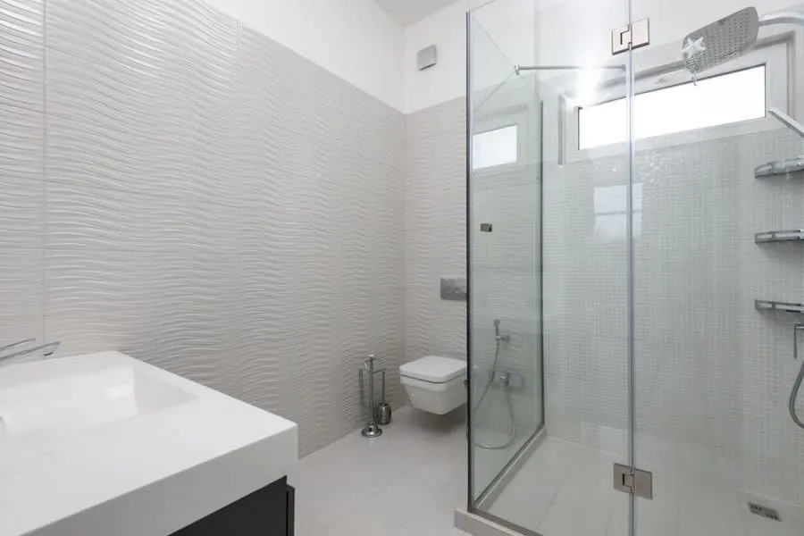Textured white walls and a corner shower enclosure in a compact bathroom
