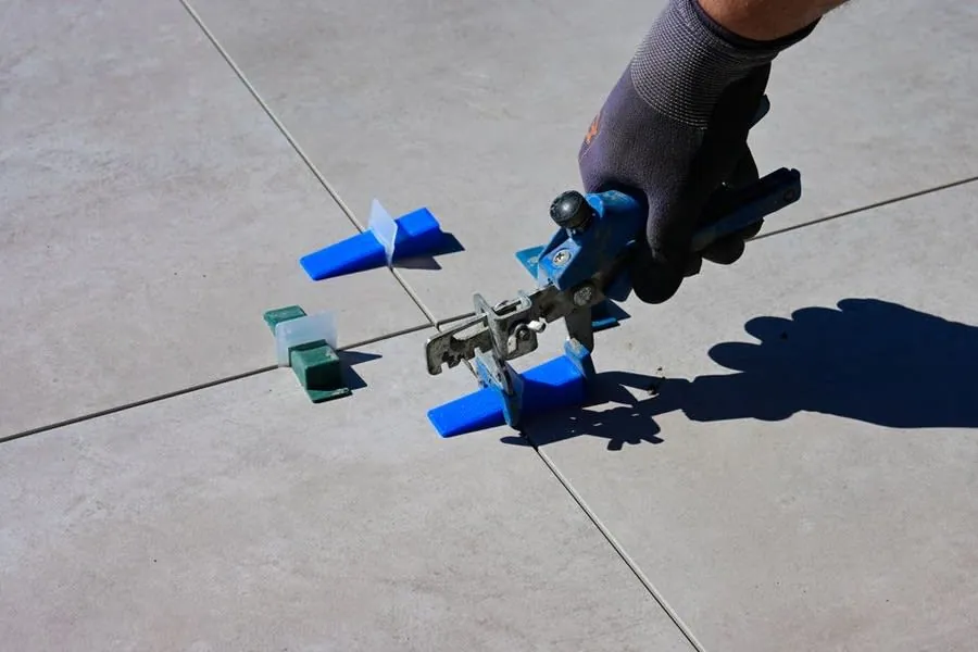 A gloved hand setting wall tiles with spacers and a levelling tool in a small room