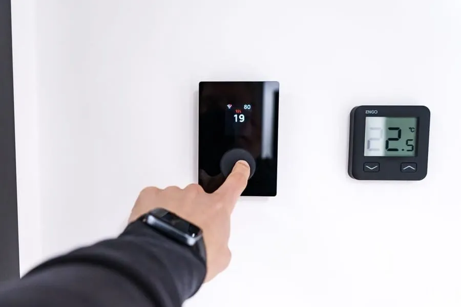 Hand adjusting a modern wall-mounted heating thermostat
