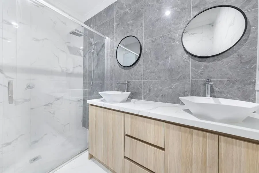 Walk-in shower alongside twin counter-top basins on an oak vanity