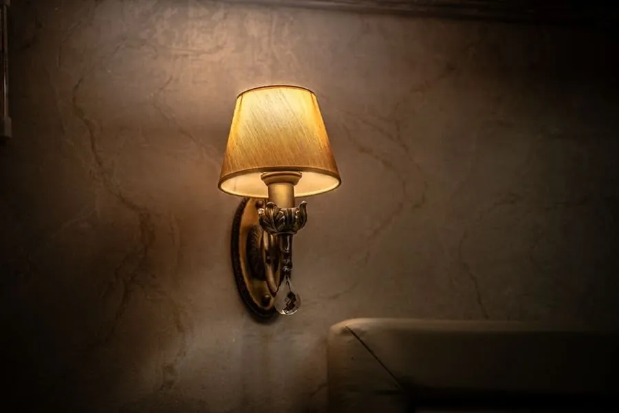 A warm-toned fabric-shade wall sconce against a stone wall