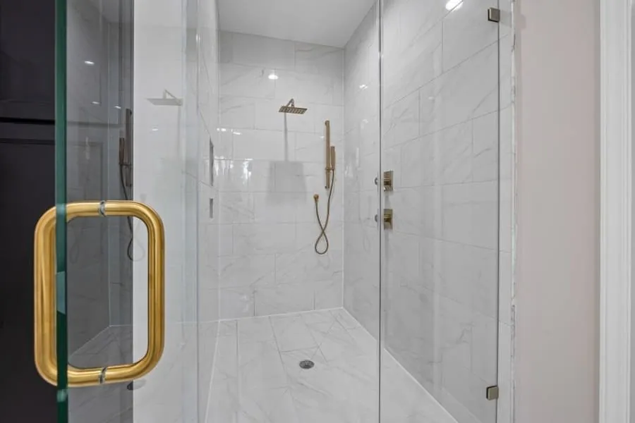 Brass shower door handle on a frameless marble-lined walk-in shower